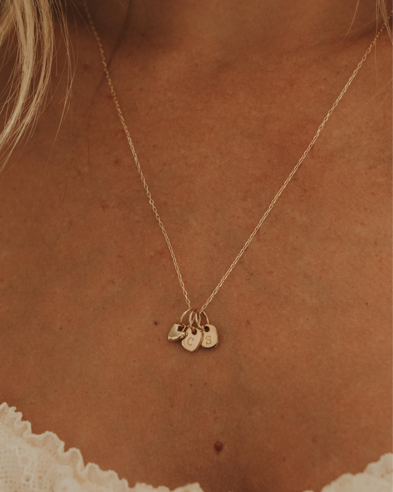 A delicate gold chain necklace with three small hanging charms, worn on a model's neck over a white lace top.