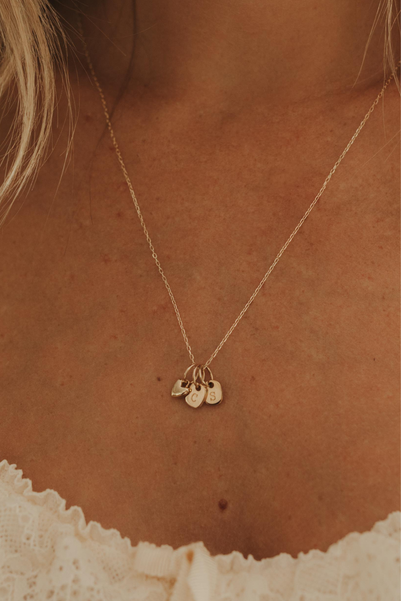 A delicate gold chain necklace with three small hanging charms, worn on a model's neck over a white lace top.