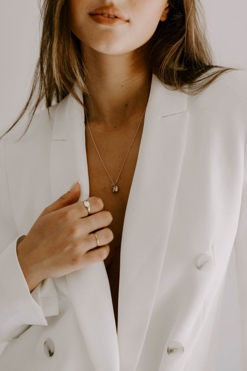 A woman in a white blazer is wearing the 50cm solid gold necklace chain with two 9ct Gold Mini Rectangular Initial Pendants on it.