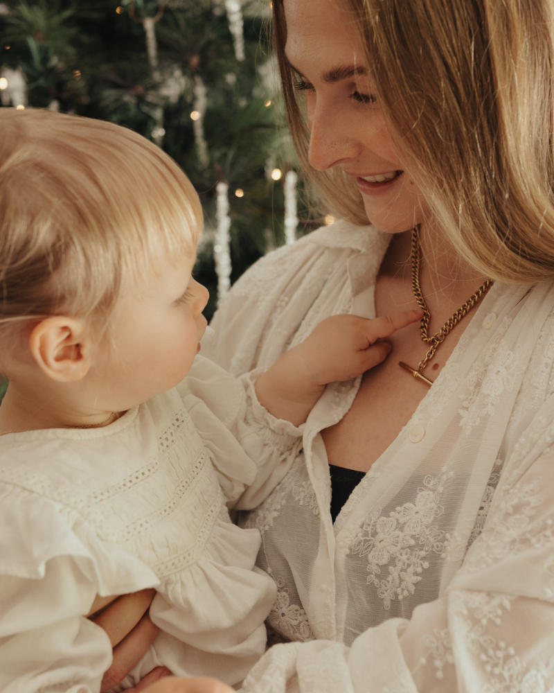 A woman is wearing a chunky fob necklace and her daughter is looking at it on her.