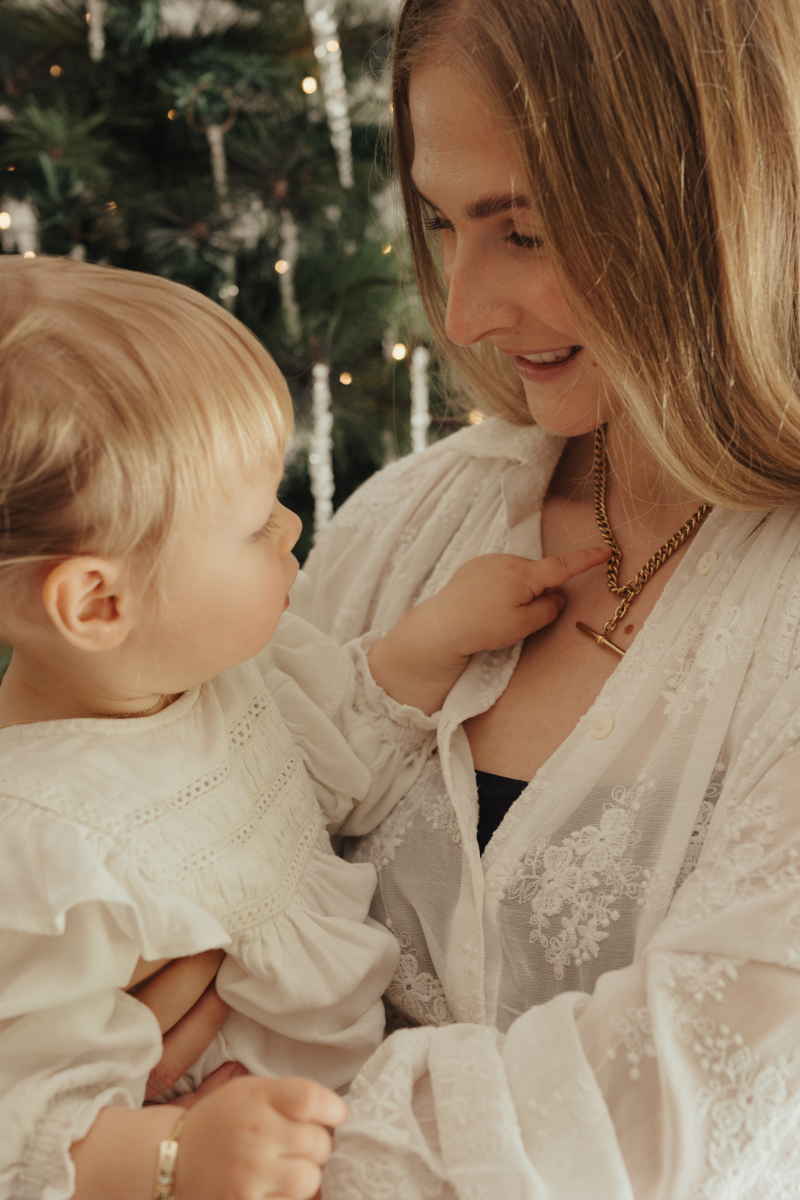 A woman is wearing a chunky fob necklace and her daughter is looking at it on her.