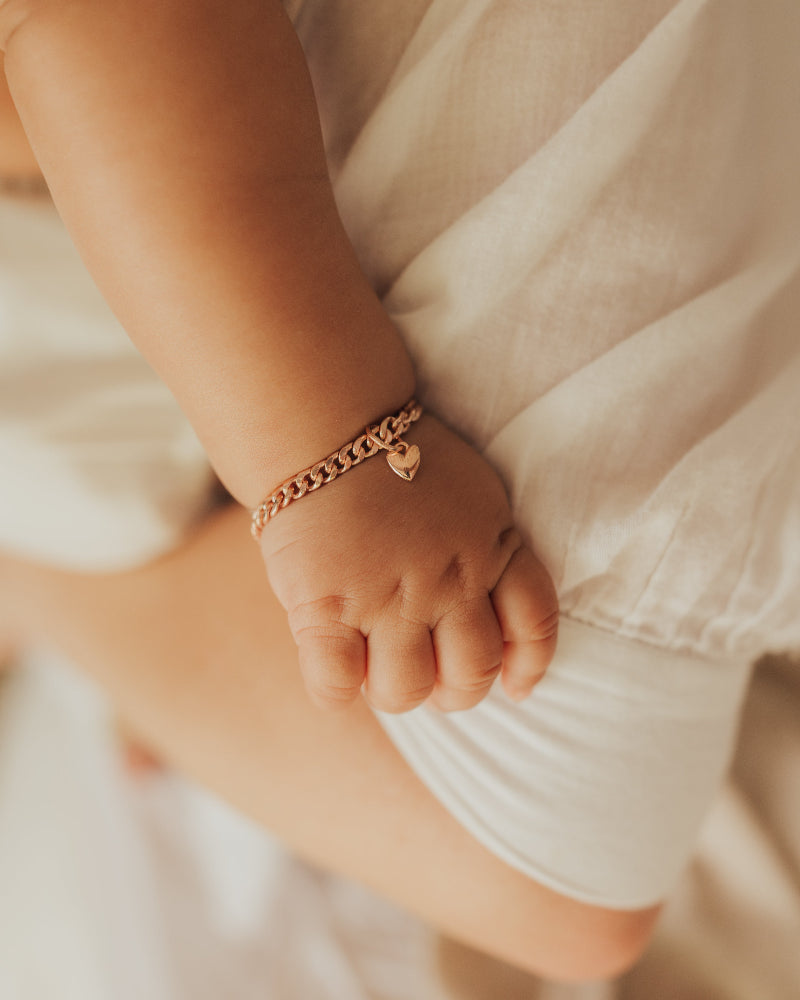 A newborn baby wrist is wearing a Cuban Link Baby bracelet with a petite heart pendant on it by Bluebird Jewellery