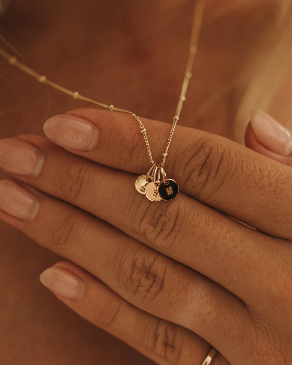 Close-up of a person wearing a delicate necklace with solid gold initial pendants and a heart pendant.