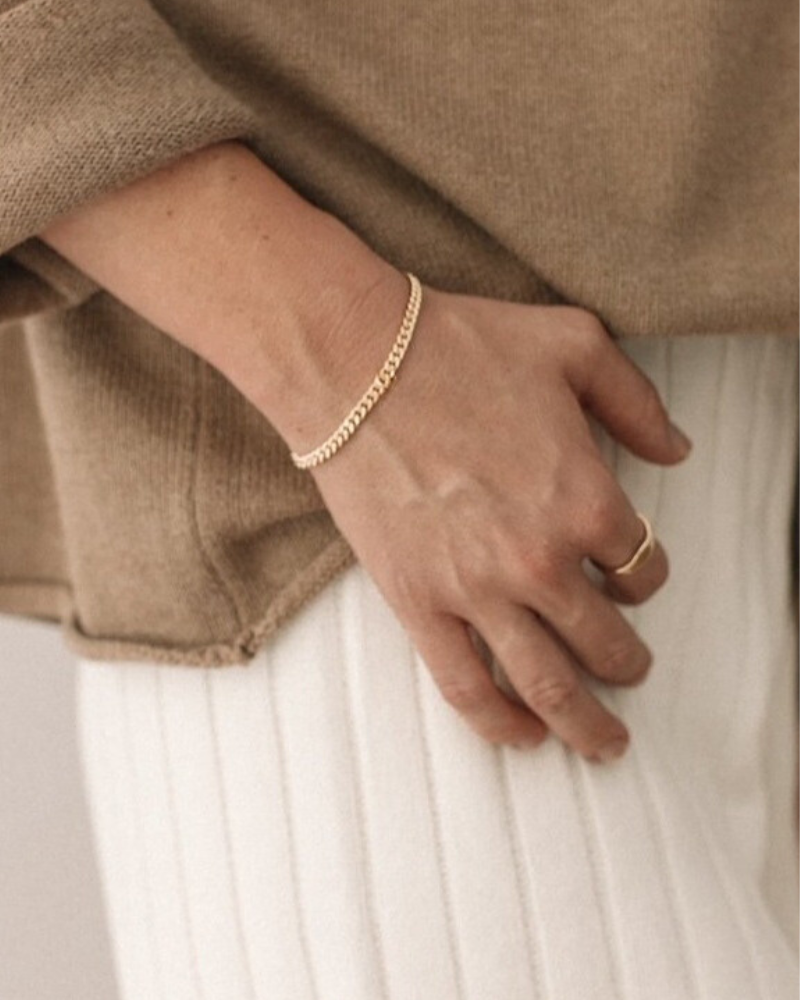 A woman wearing a gold bracelet and gold signet ring, a meaningful piece of fine jewellery designed for everyday wear by Bluebird Jewellery
