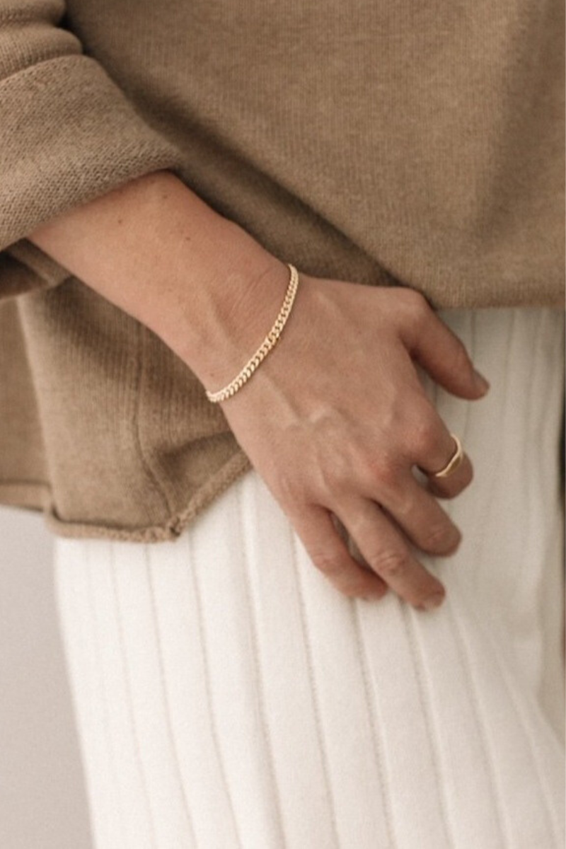 A woman wearing a gold bracelet and gold signet ring, a meaningful piece of fine jewellery designed for everyday wear by Bluebird Jewellery