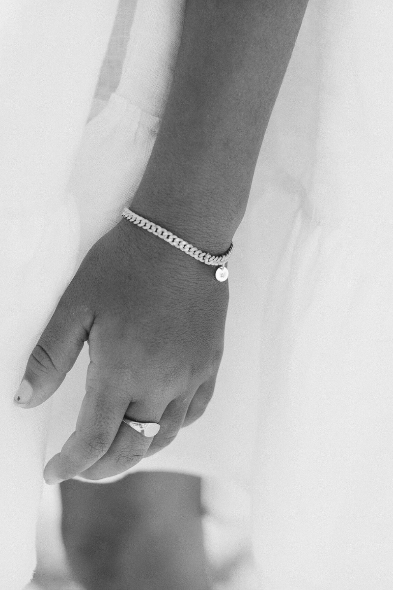 A detailed close-up of a child wearing a silver bracelet with an engraved initial pendant and a matching signet ring, crafted for timeless everyday style.
