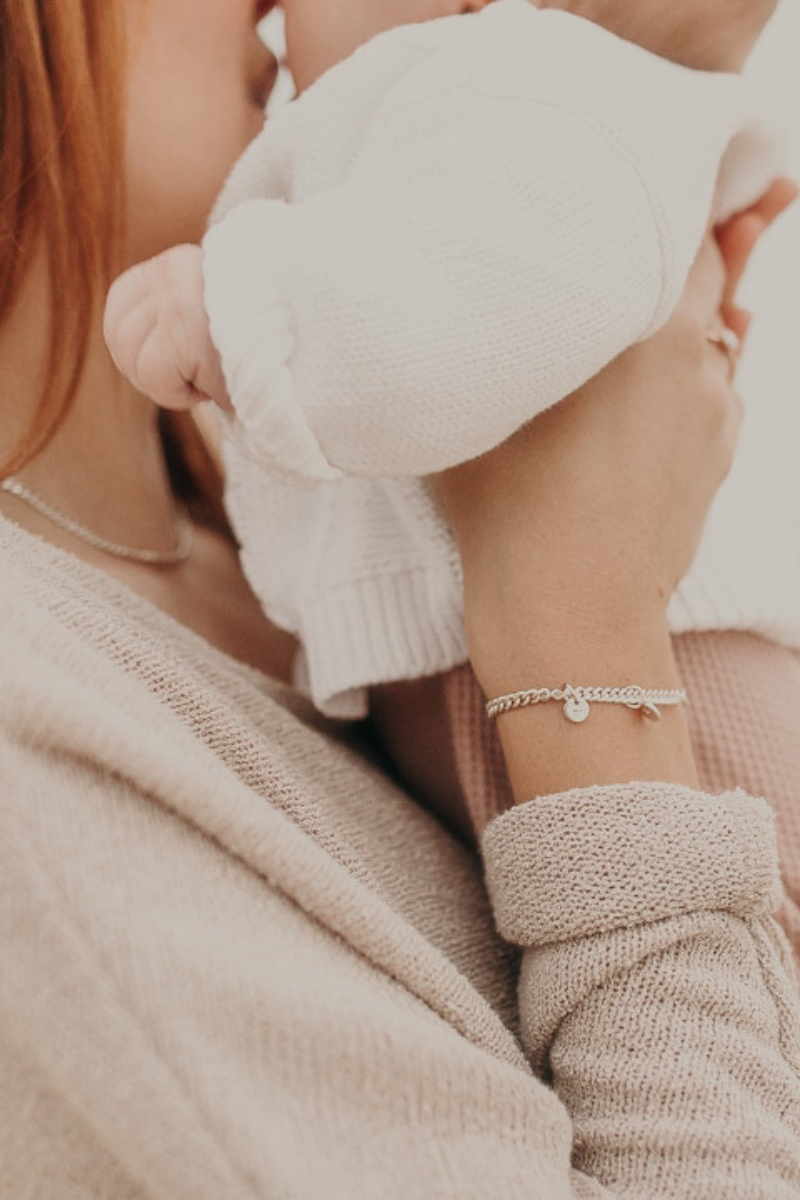 A mum carrying her child, wearing a personalised silver bracelet with engraved initials, designed to celebrate love and family.