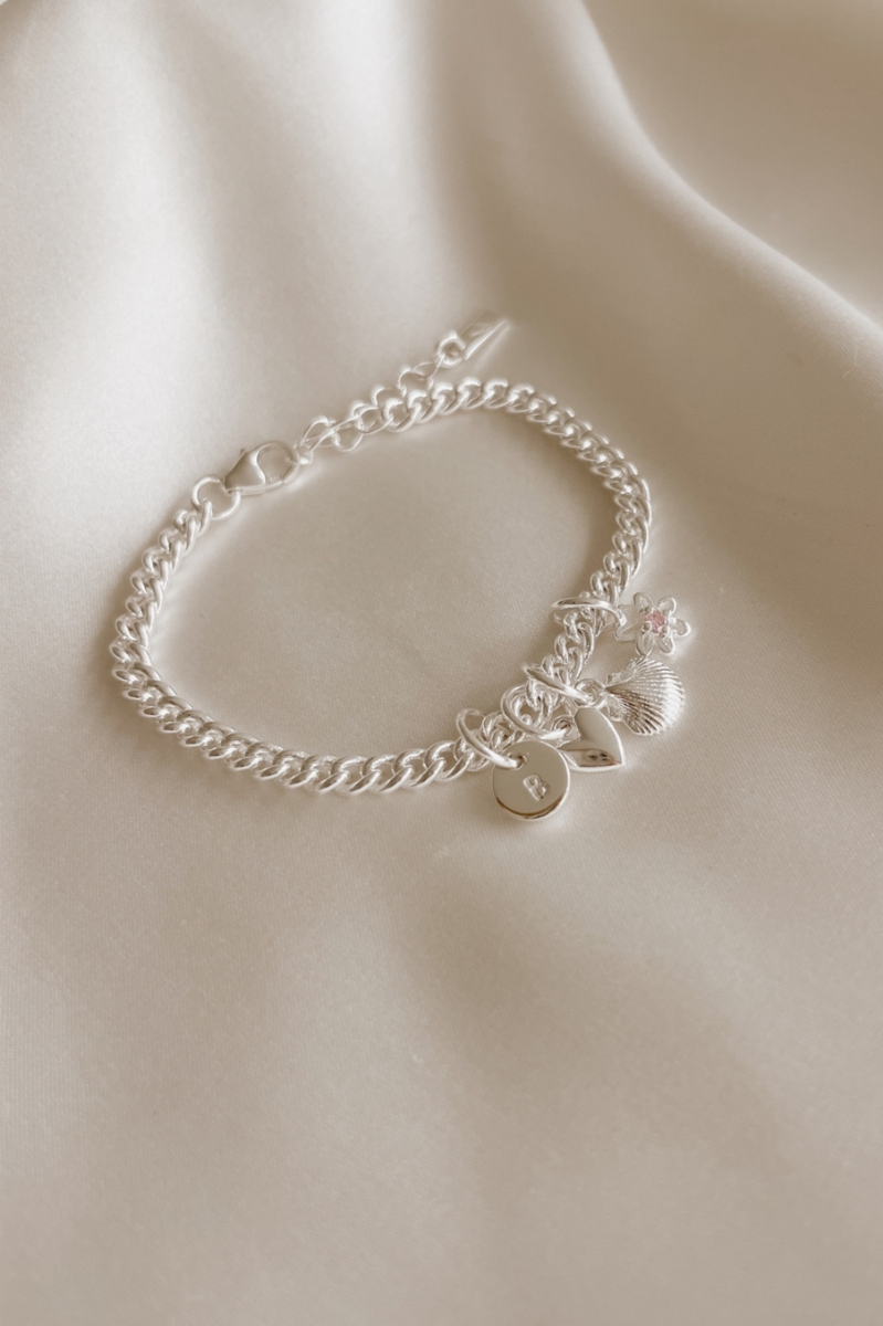 A close-up of a handcrafted silver bracelet featuring engraved pendants and charms, designed as timeless personalised jewellery by Bluebird Co