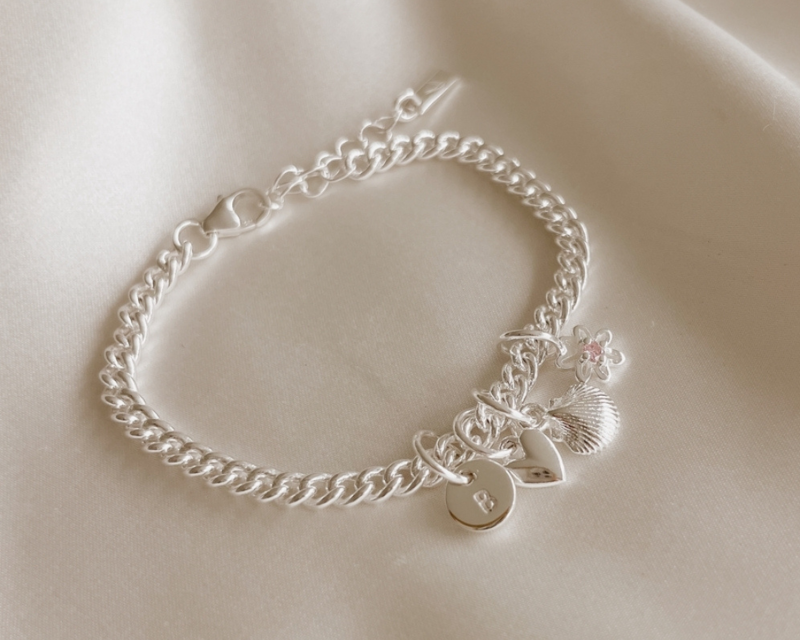 A close-up of a handcrafted silver bracelet featuring engraved pendants and charms, designed as timeless personalised jewellery by Bluebird Co
