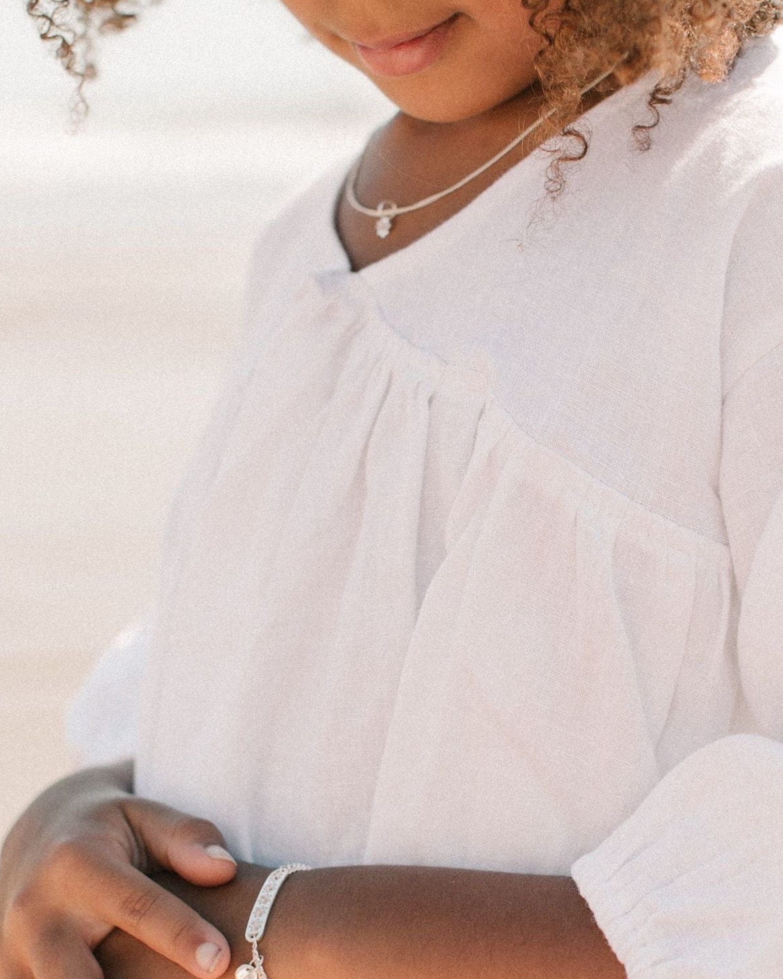 A child wearing a silver Daisy Bracelet by Bluebird Jewellery, featuring five hand-drawn daisies with pink cubic zirconia centres, crafted as a feminine and floral fine jewellery piece along with an initial pendant that represents her name.