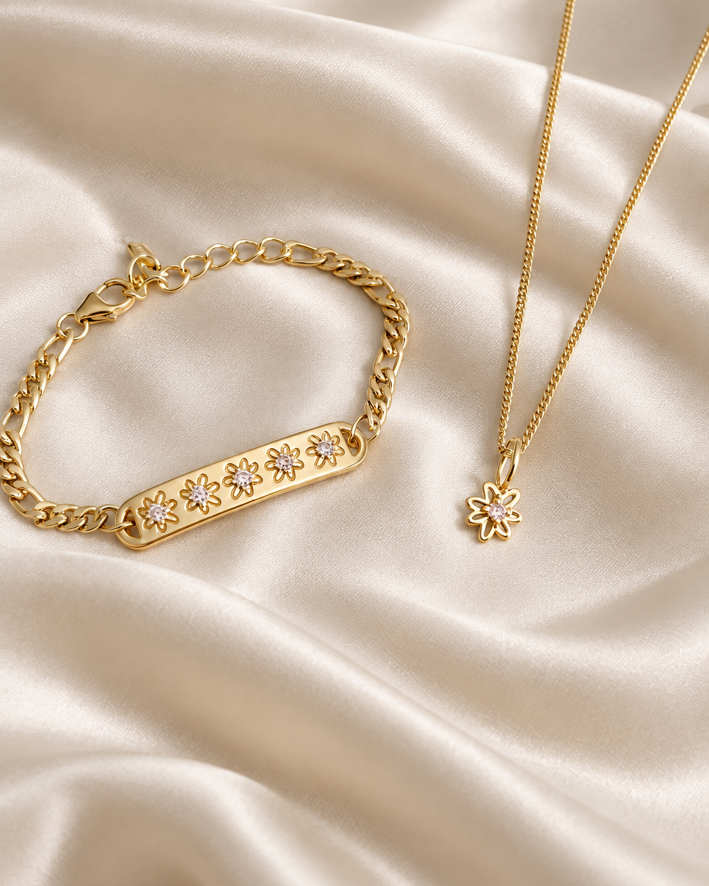 Gold jewelry set featuring a bar bracelet with floral crystal details and a matching flower pendant necklace, displayed on a cream satin fabric background.