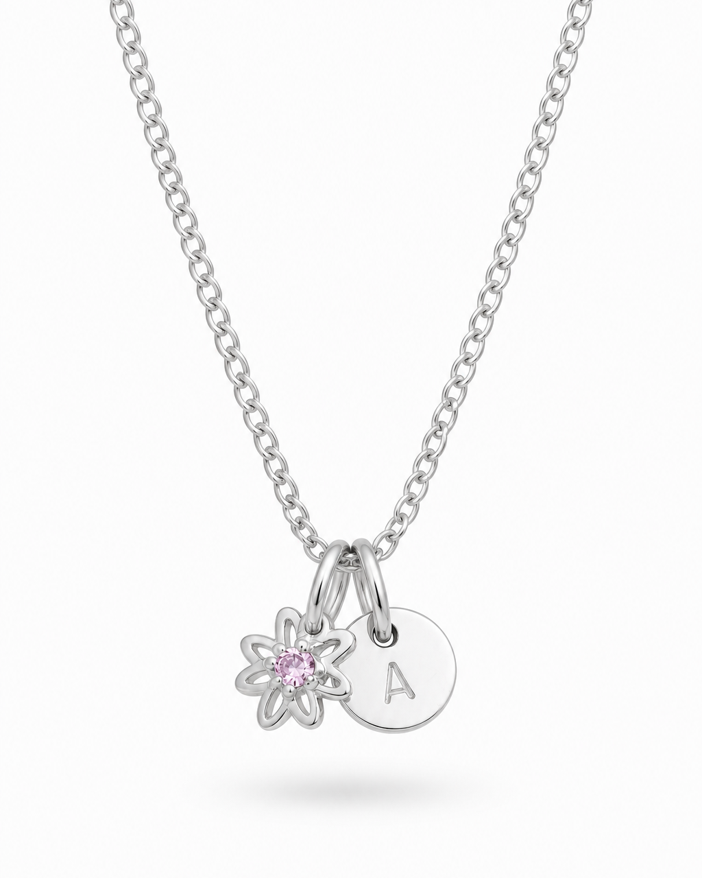 A silver chain necklace with two charms: a small flower charm with a pink gemstone and a round disc charm engraved with the letter 'A', shown on a light gray background.