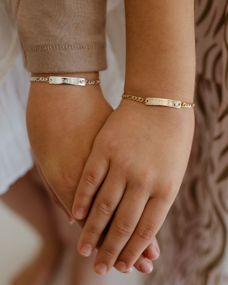 Two children wearing engraved gold bracelets—personalised friendship jewellery for siblings, babies, or kids by Bluebird Jewellery.