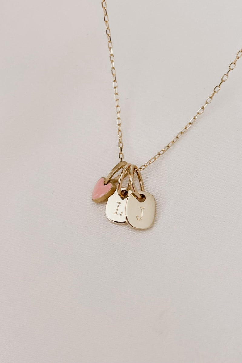 A pink Darling Pendant is on a solid gold chain alongside two mini rectangular pendants also in solid gold