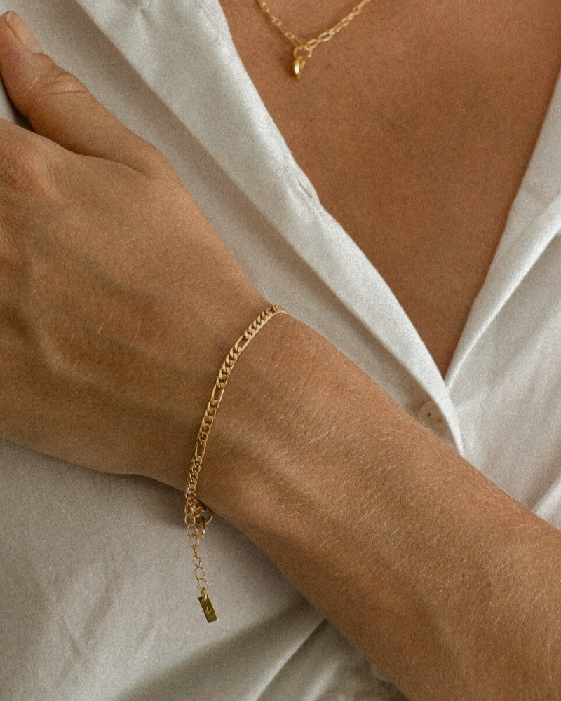 A woman wears a Bluebird Jewellery Figaro Bracelet in gold, a timeless fine chain design with adjustable sizing, crafted as an elegant everyday piece.