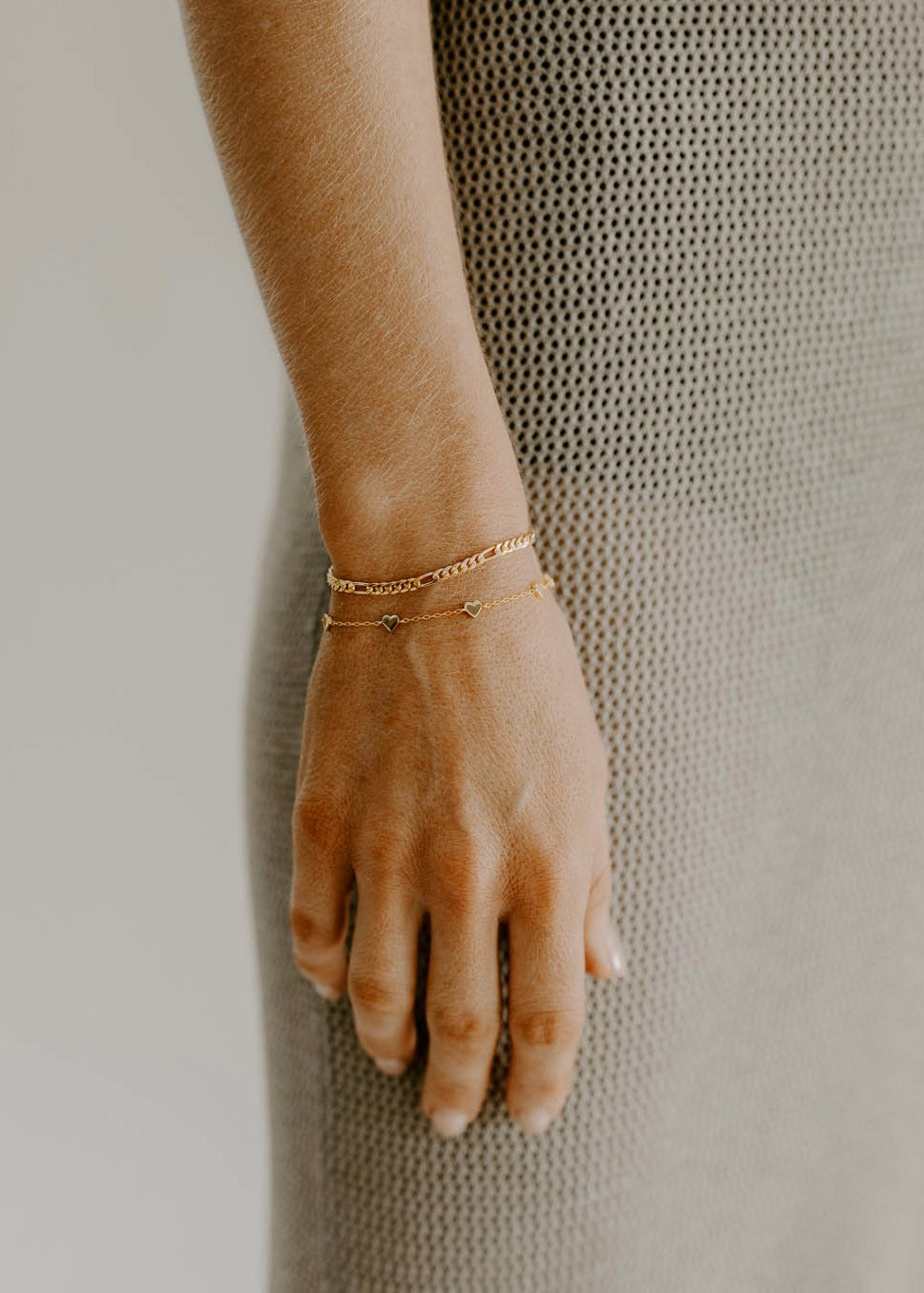 A rose gold figaro bracelet and Rose Gold Heart Bracelet are worn together.