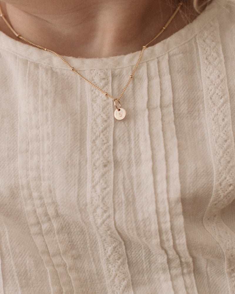 A child is wearing the child length Gold petite Personalised necklace with a solid gold letter pendant that reflects the first letter of her name.