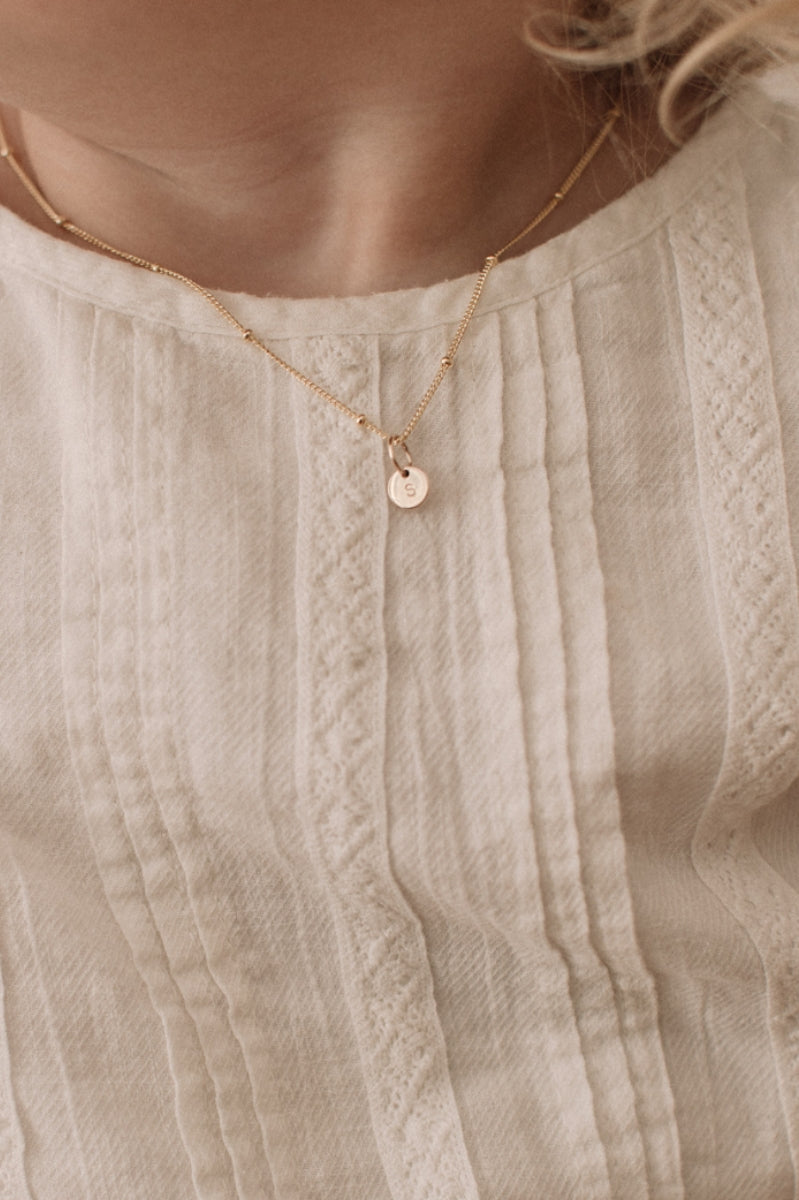A child is wearing the child length Gold petite Personalised necklace with a solid gold letter pendant that reflects the first letter of her name.