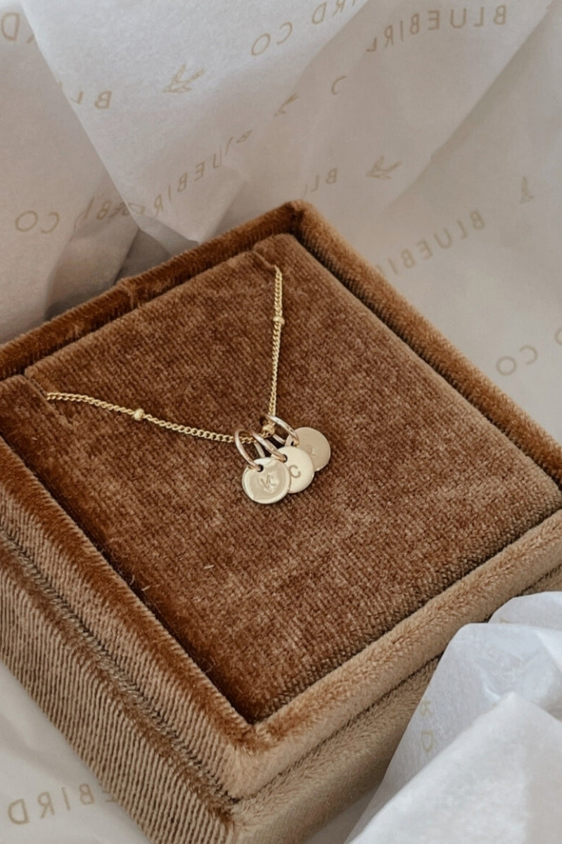 A ball chain necklace is shown in a bluebird co gift box. The necklace chee at in has three personalised pendants on it.