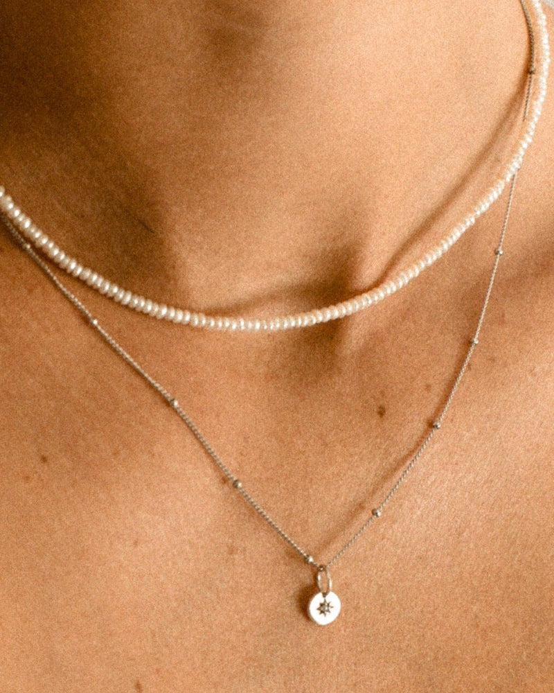 A woman is wearing a Freshwater Pearl necklace layered with a Vintage Pearl Necklace. The two necklaces both feature natural pearls and look both modern and elegant on the woman’s neckline.