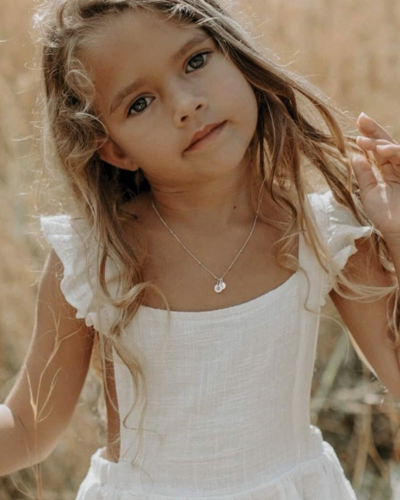 A young girl is standing in a field and is wearing a white dress with a Vintage Pearl necklace that has a personalised initial pendant added to it with her letter pendant.