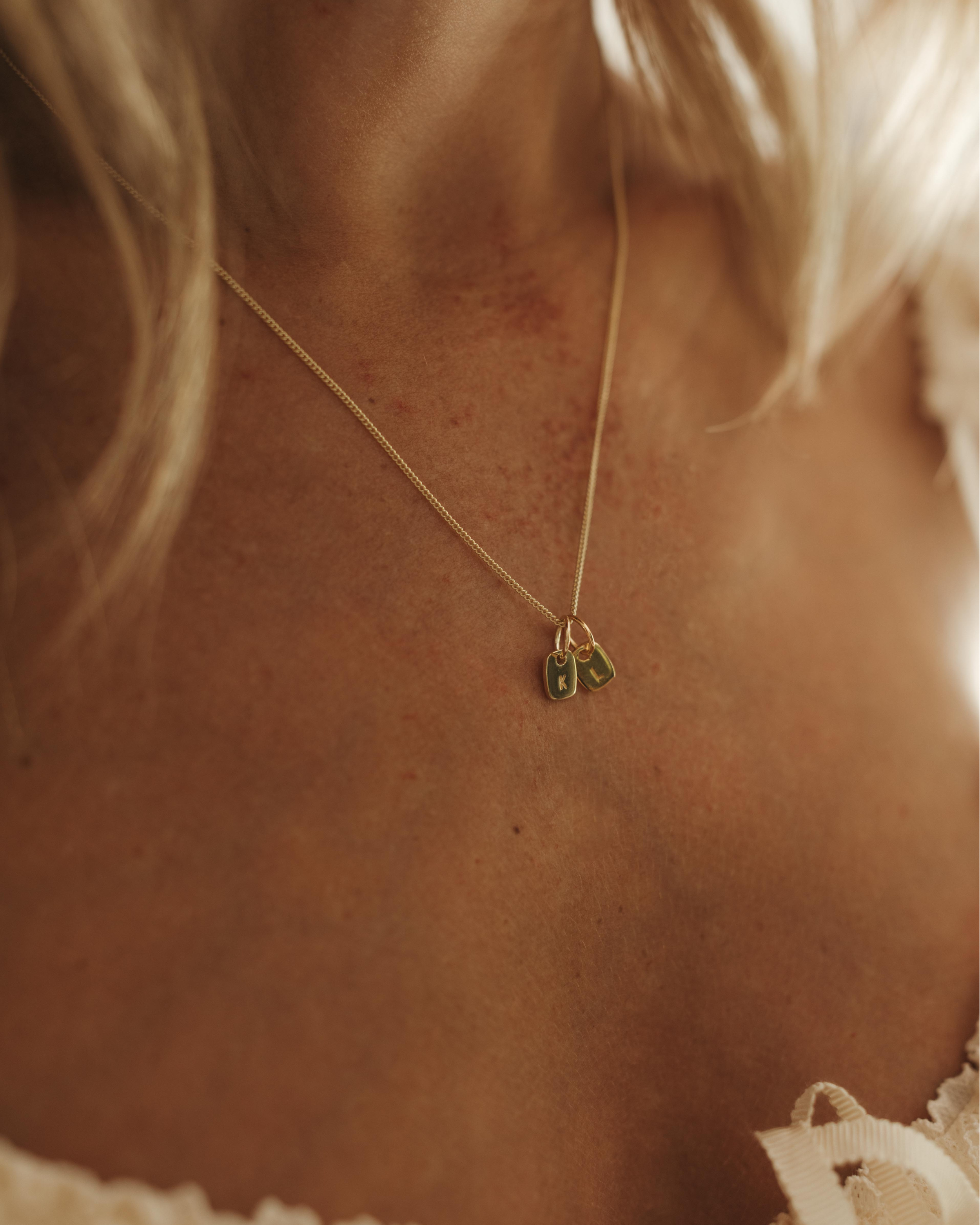 Woman wearing a gold necklace with a heart pendant, smiling.