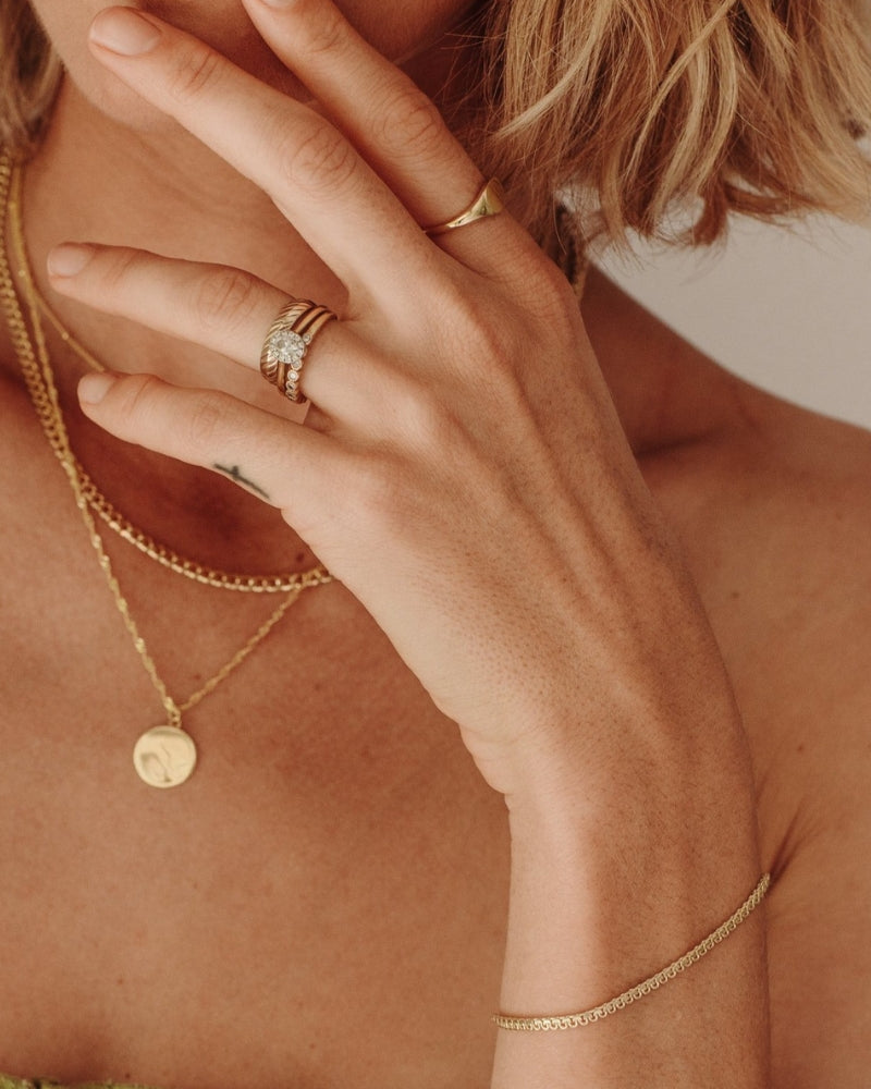 A close-up of a woman wearing layered gold necklaces including a Lace Chain, complemented by minimalist matching rings, styled as refined modern jewellery by Bluebird Co