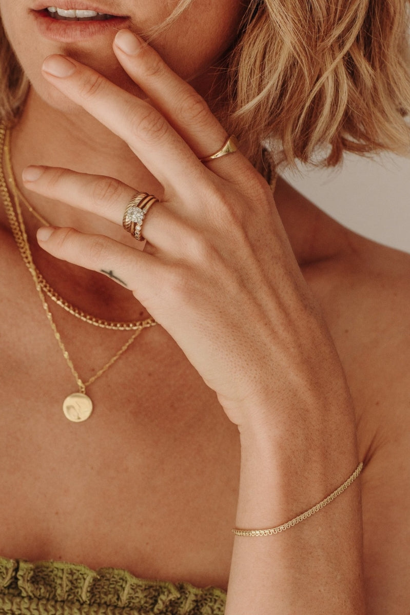 A close-up of a woman wearing layered gold necklaces including a Lace Chain, complemented by minimalist matching rings, styled as refined modern jewellery.
