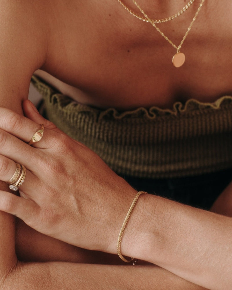 A close-up of a woman wearing layered gold necklaces including a Lace Chain, complemented by minimalist matching rings, styled as refined modern jewellery by Bluebird Co