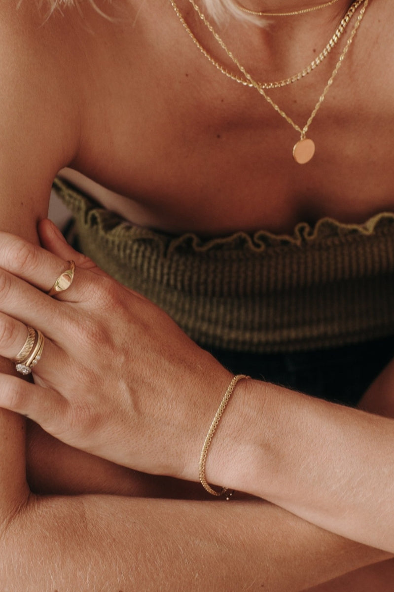 A close-up of a woman wearing layered gold necklaces including a Lace Chain, complemented by minimalist matching rings, styled as refined modern jewellery.