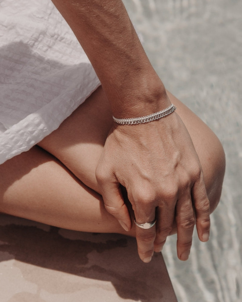 A close-up image capturing a woman’s hand wearing a Lace Chain Bracelet and matching gold signet ring, styled with refined simplicity by Bluebird Jewellery