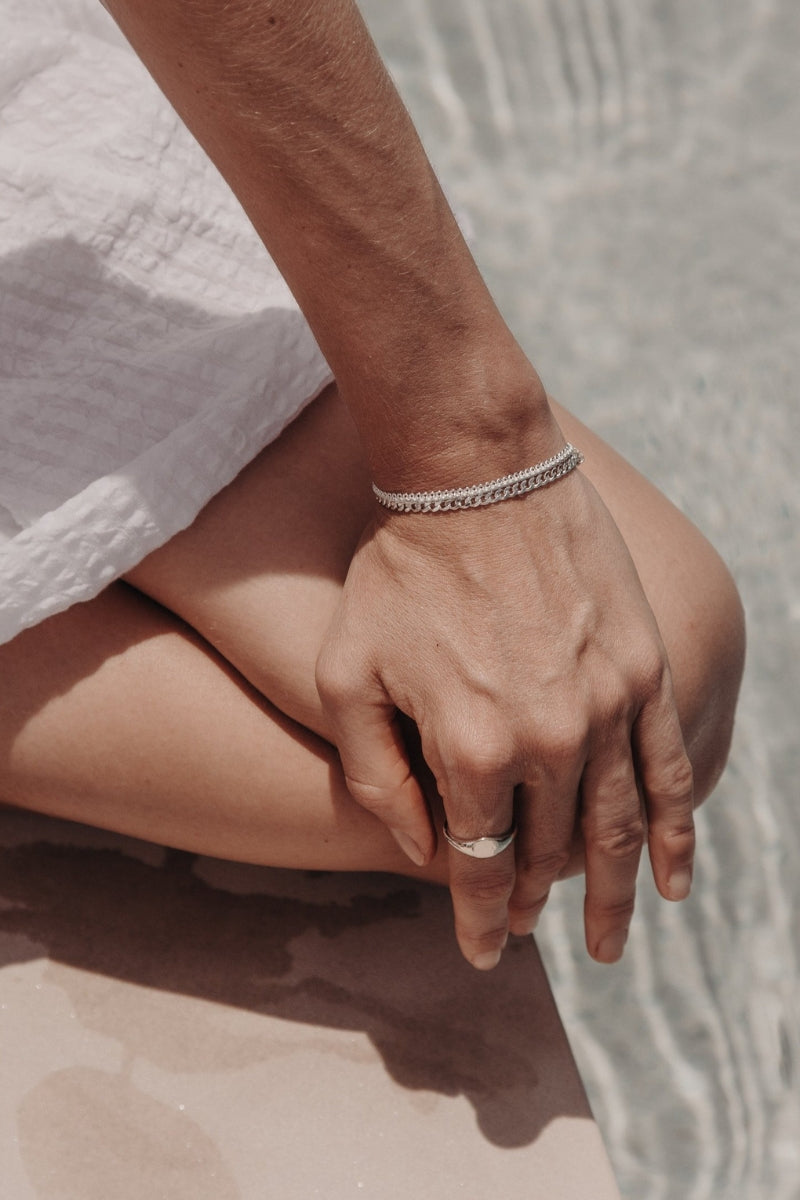 A close-up image capturing a woman’s hand wearing a Lace Chain Bracelet and matching gold signet ring, styled with refined simplicity