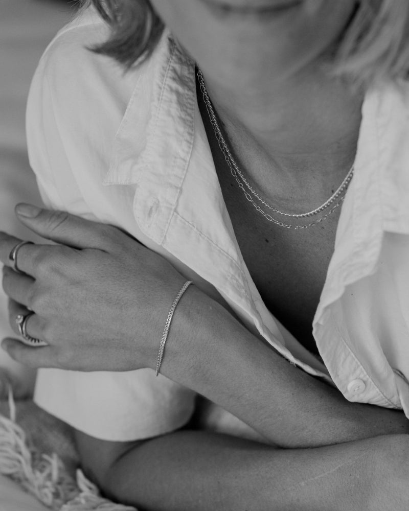 A close-up of a woman wearing silver necklaces including a Lace Chain, complemented by minimalist matching rings, crafted in timeless fine jewellery style by Bluebird Co