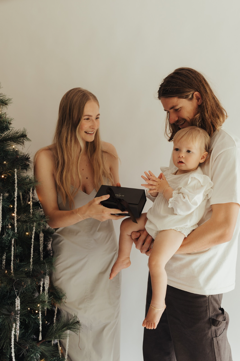 Baby is wearing a gold anklet and is being held by her dad as her family stands at the Christmas tree. The anklet has a lace chain style.