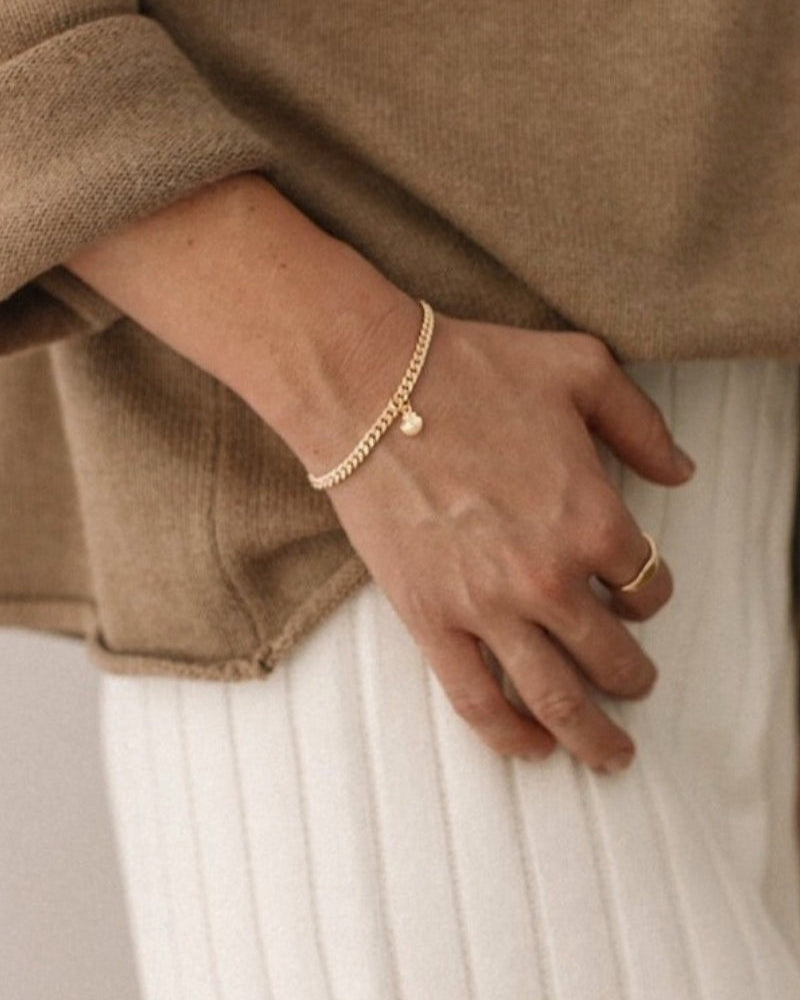 A woman wearing a gold Cuban Link Chain Bracelet with a mermaid shell charm, paired with a matching signet ring for a refined, modern look by Bluebird Jewellery.