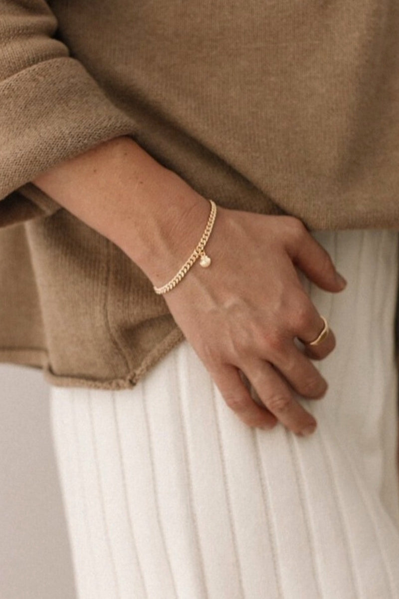 A woman wearing a gold Cuban Link Chain Bracelet with a mermaid shell charm, paired with a matching signet ring for a refined, modern look by Bluebird Jewellery.