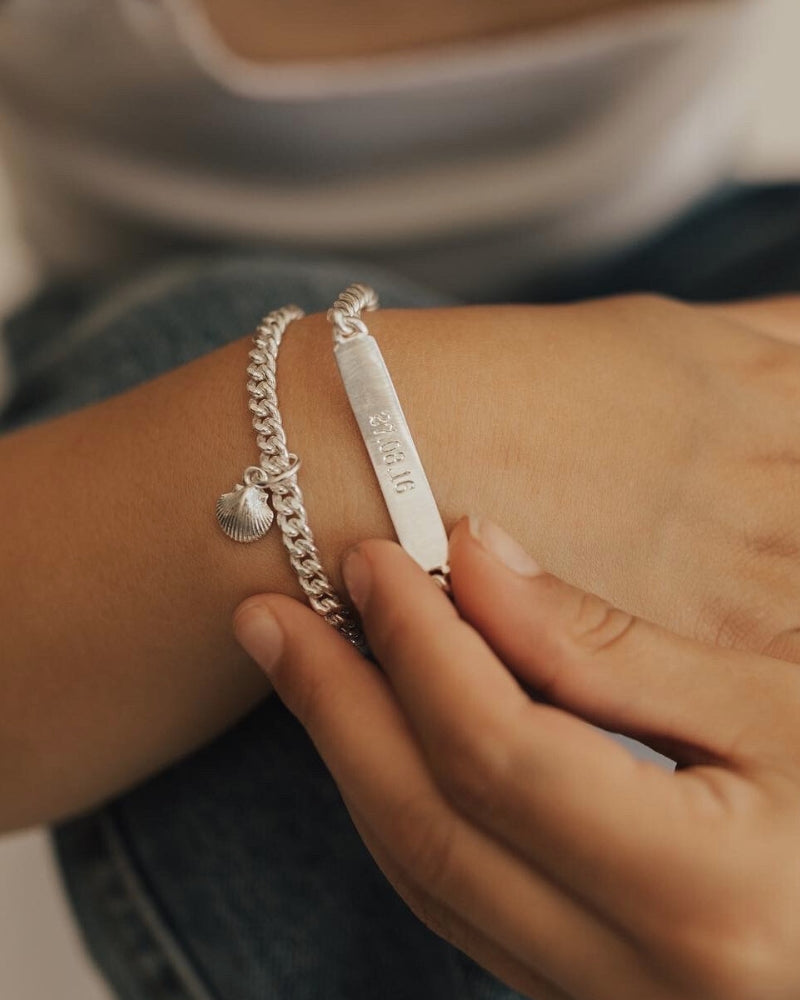 A delicate image of a child wearing a gold Cuban Link Chain Bracelet with a mermaid shell charm and matching Signature Bracelet, symbolising elegance and connection.