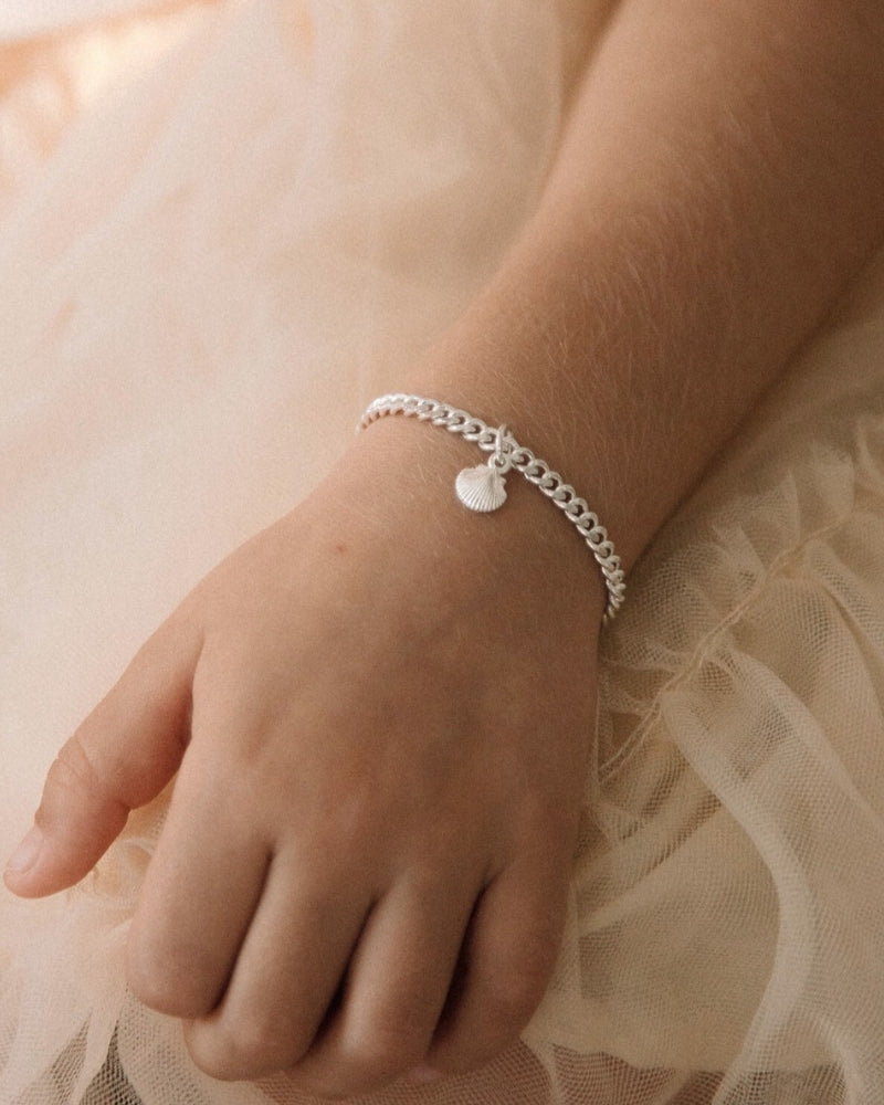 Perfectly simple and beautiful. The Little Mermaid Cuban Link bracelet in child length with a mini shell pendant is worn by a young girl with a peach tulle tutu.