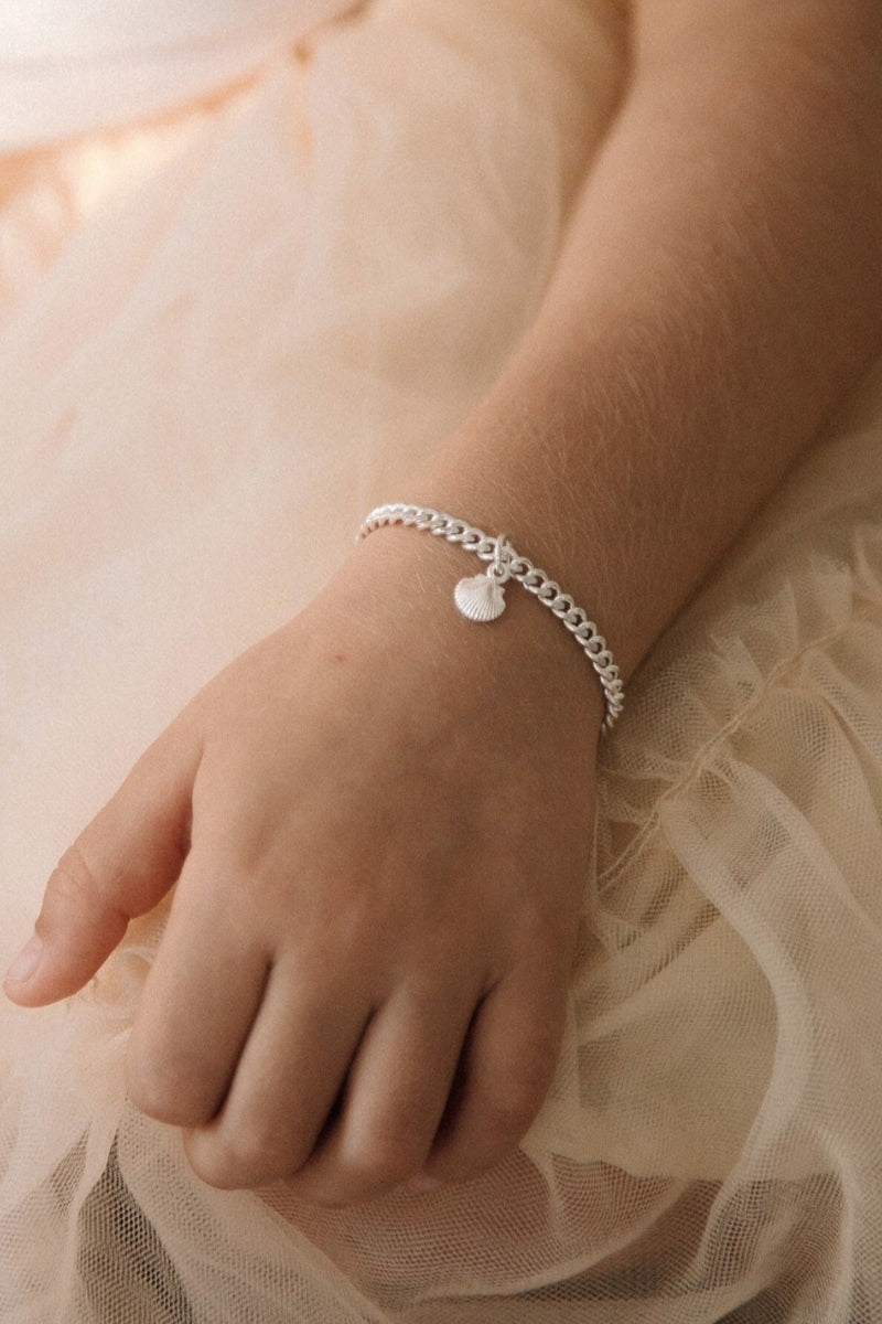 Perfectly simple and beautiful.  The Little Mermaid Cuban Link bracelet in child length with a mini shell pendant is worn by a young girl with a peach tulle tutu.