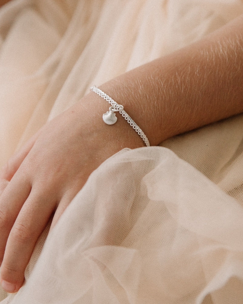 A child is wearing a child sized Little Mermaid Lace Chain Bracelet with a mini shell pendant on it