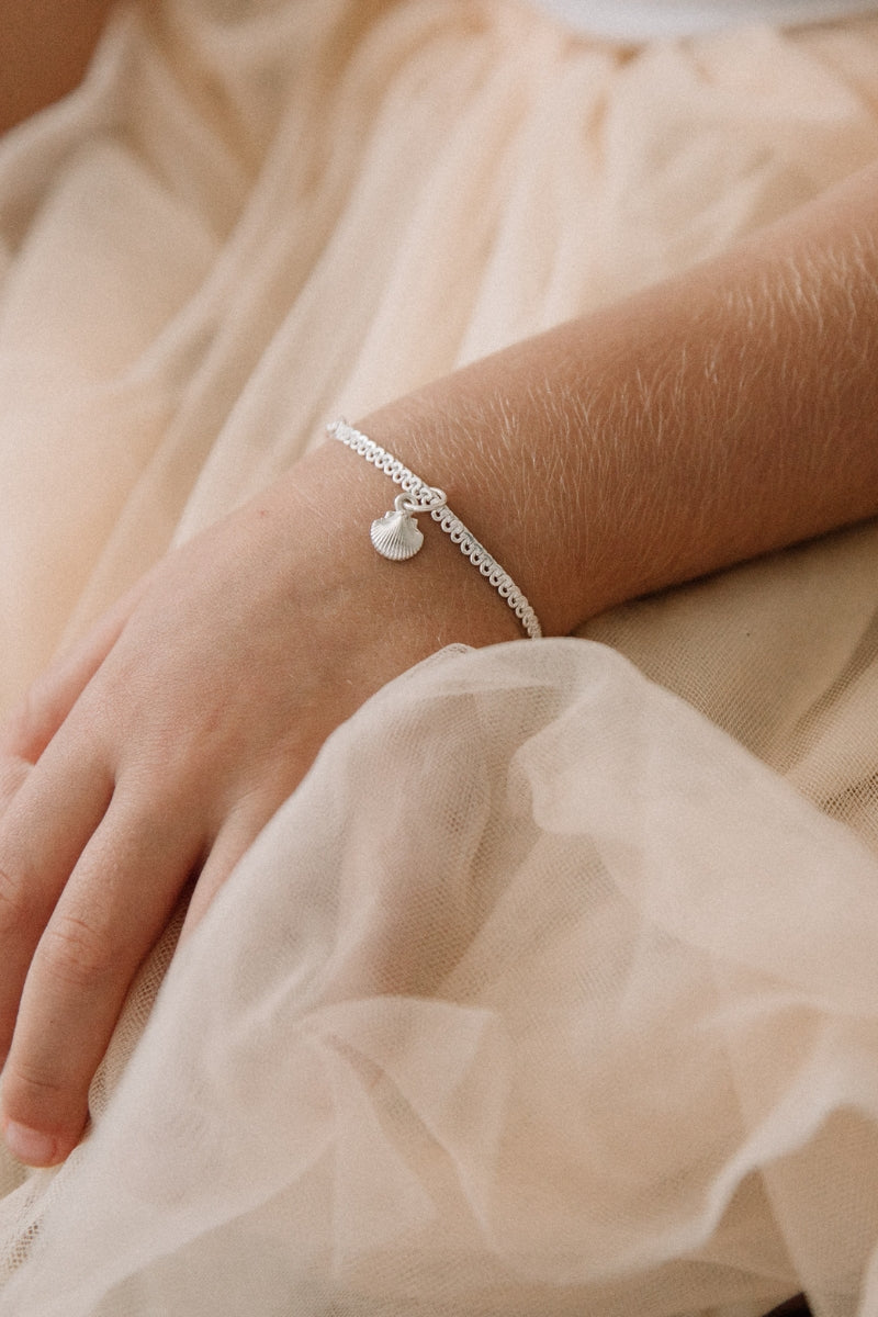 A child is wearing a child sized Little Mermaid Lace Chain Bracelet with a mini shell pendant on it
