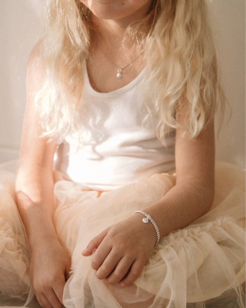 A child wearing a silver Lace Chain Bracelet with a mermaid shell, crafted as a meaningful keepsake piece.