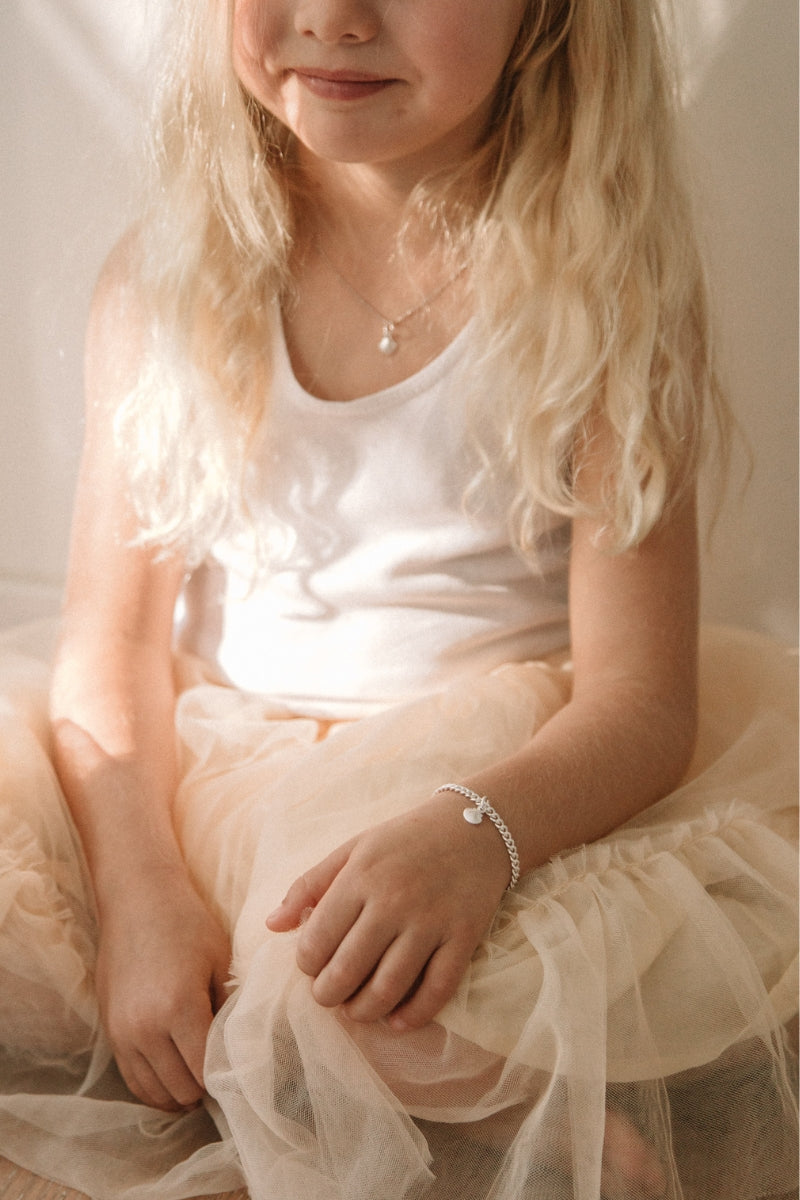 A child wearing a silver Lace Chain Bracelet with a mermaid shell, crafted as a meaningful keepsake piece.