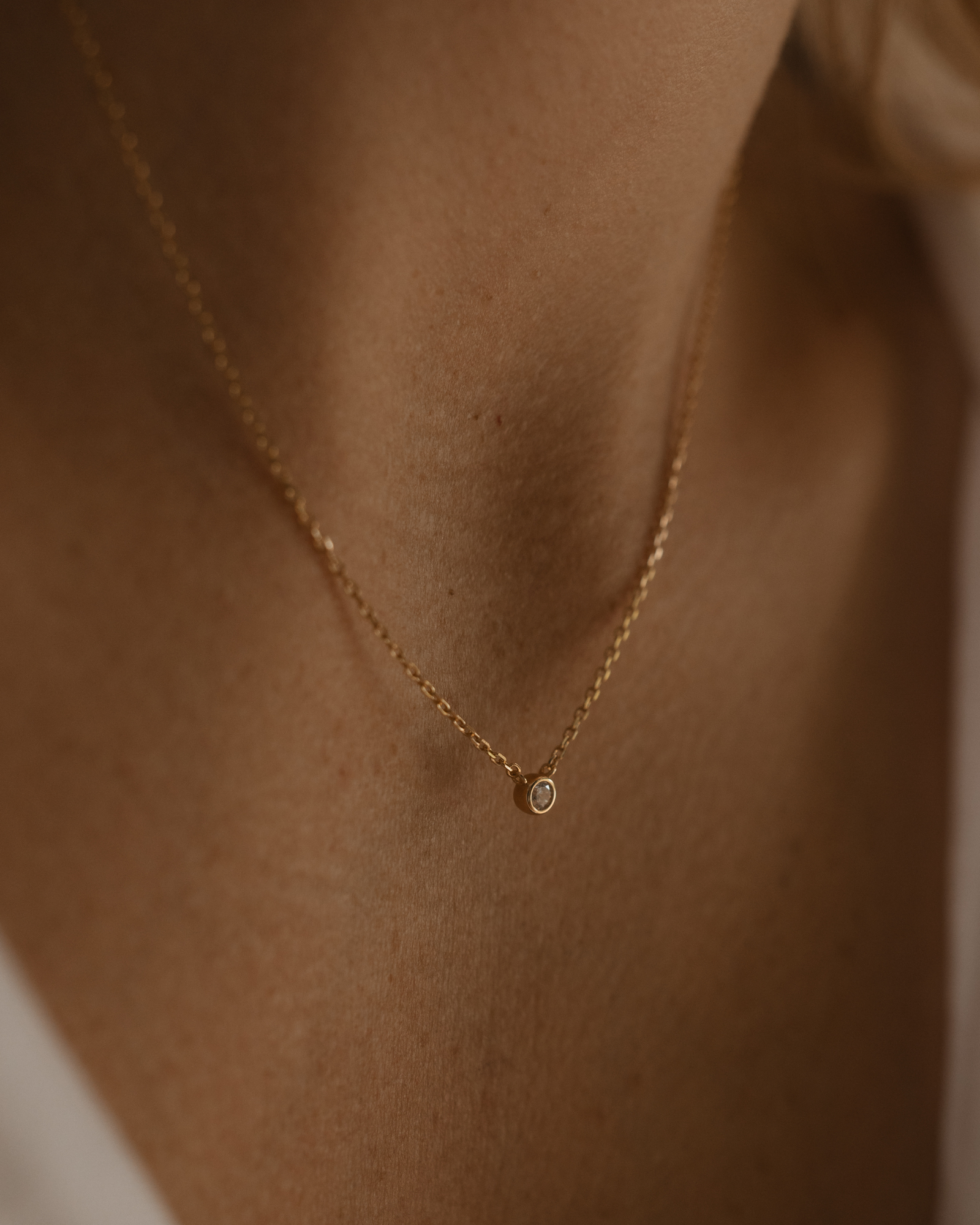 A woman wearing the Lumé Necklace by Bluebird Jewellery, a delicate gold pendant designed to reflect light and celebrate life’s special milestones.
