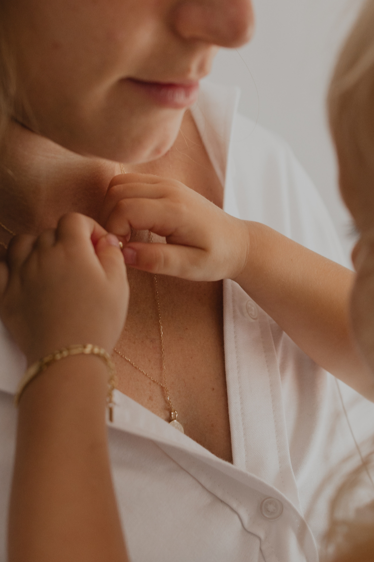 A close-up photo of mum with baby wearing a Lumé Necklace by Bluebird Jewellery, inspired by the French word for ‘light,’ crafted as a radiant symbol of warmth and kindness.