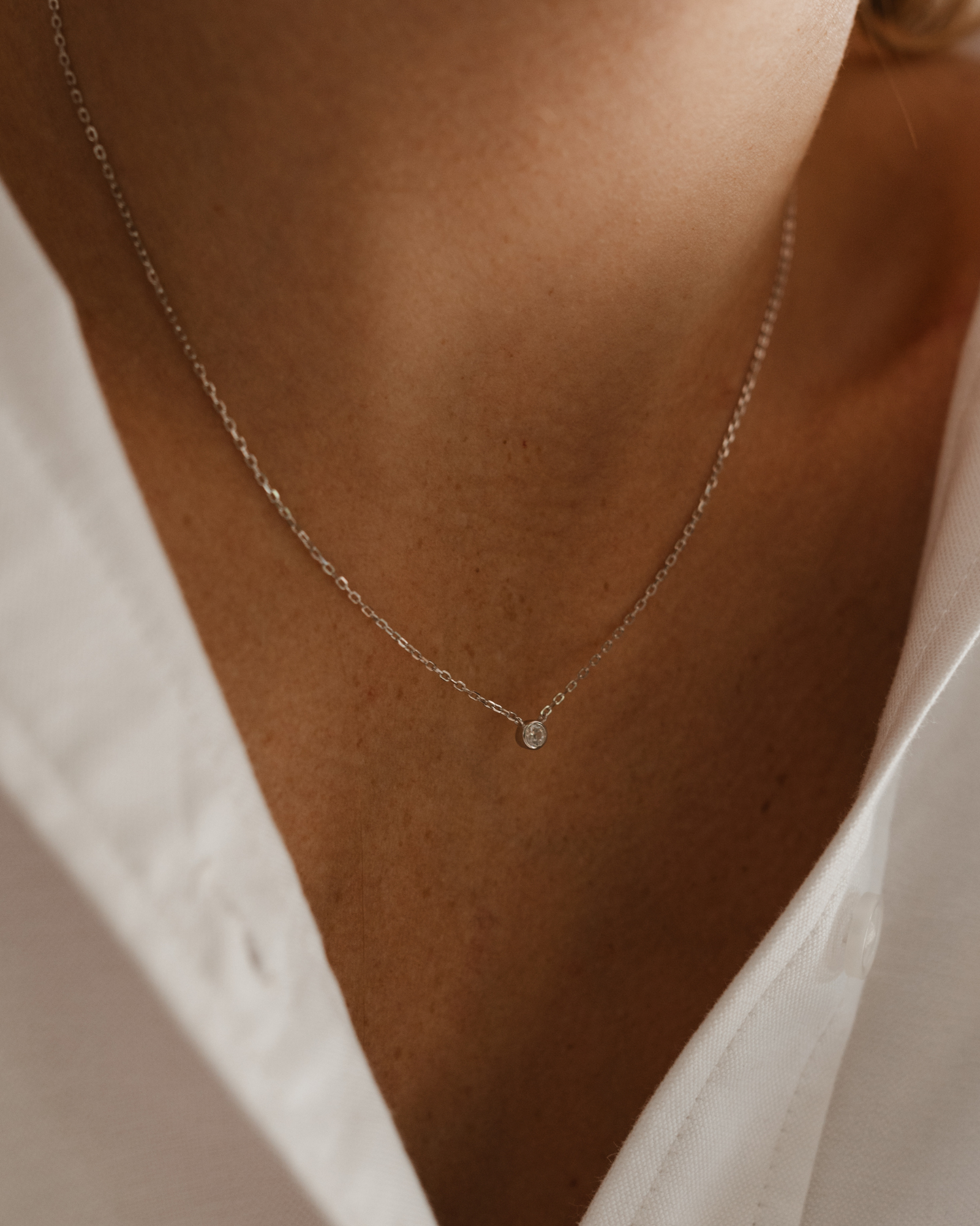 A close-up photo of a woman wearing the Lumé Necklace by Bluebird Jewellery, inspired by the French word for ‘light,’ crafted as a radiant symbol of warmth and kindness.