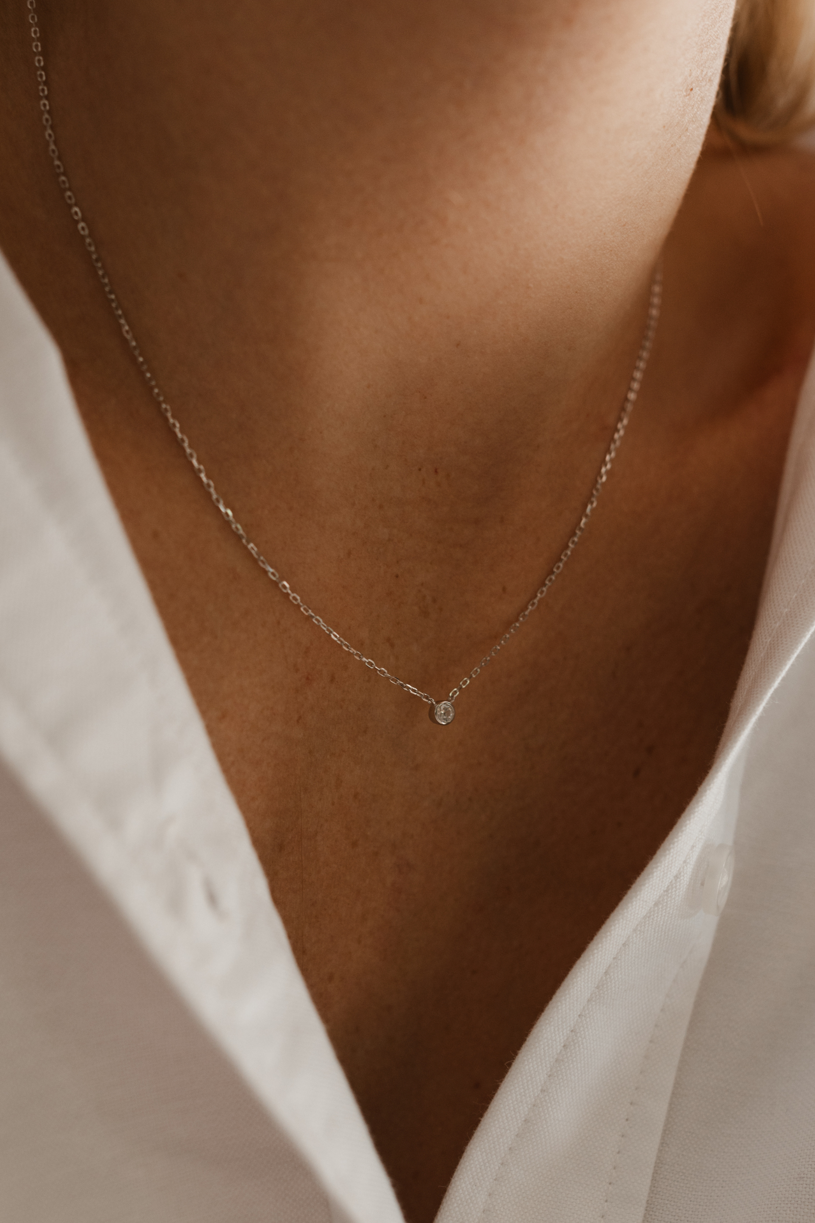 A close-up photo of a woman wearing the Lumé Necklace by Bluebird Jewellery, inspired by the French word for ‘light,’ crafted as a radiant symbol of warmth and kindness.
