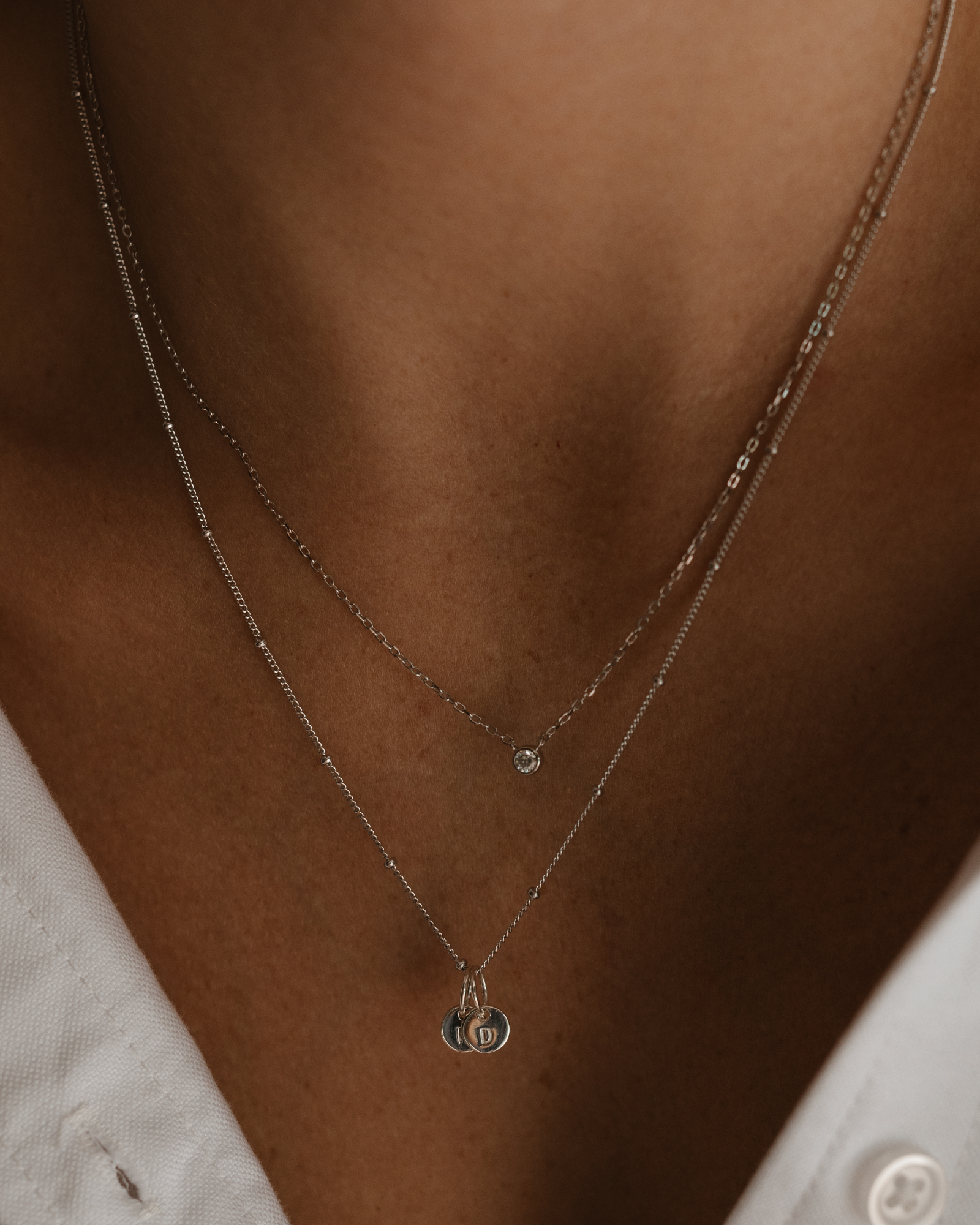 A woman wearing a silver Lumé Necklace by Bluebird Jewellery, inspired by the French word for ‘light’ and crafted as a meaningful fine jewellery gift. With matching personalised necklace with engraved pendants.