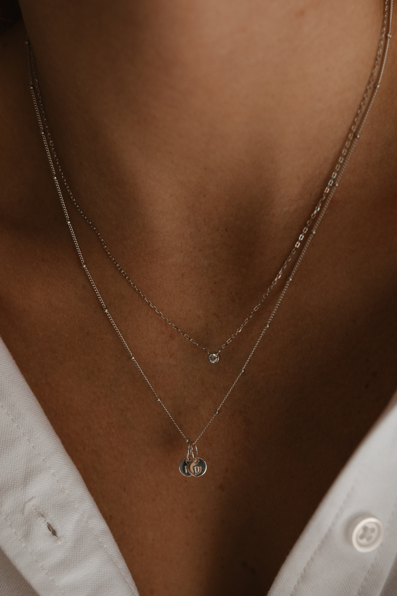 A woman wearing a silver Lumé Necklace by Bluebird Jewellery, inspired by the French word for ‘light’ and crafted as a meaningful fine jewellery gift. With matching personalised necklace with engraved pendants.