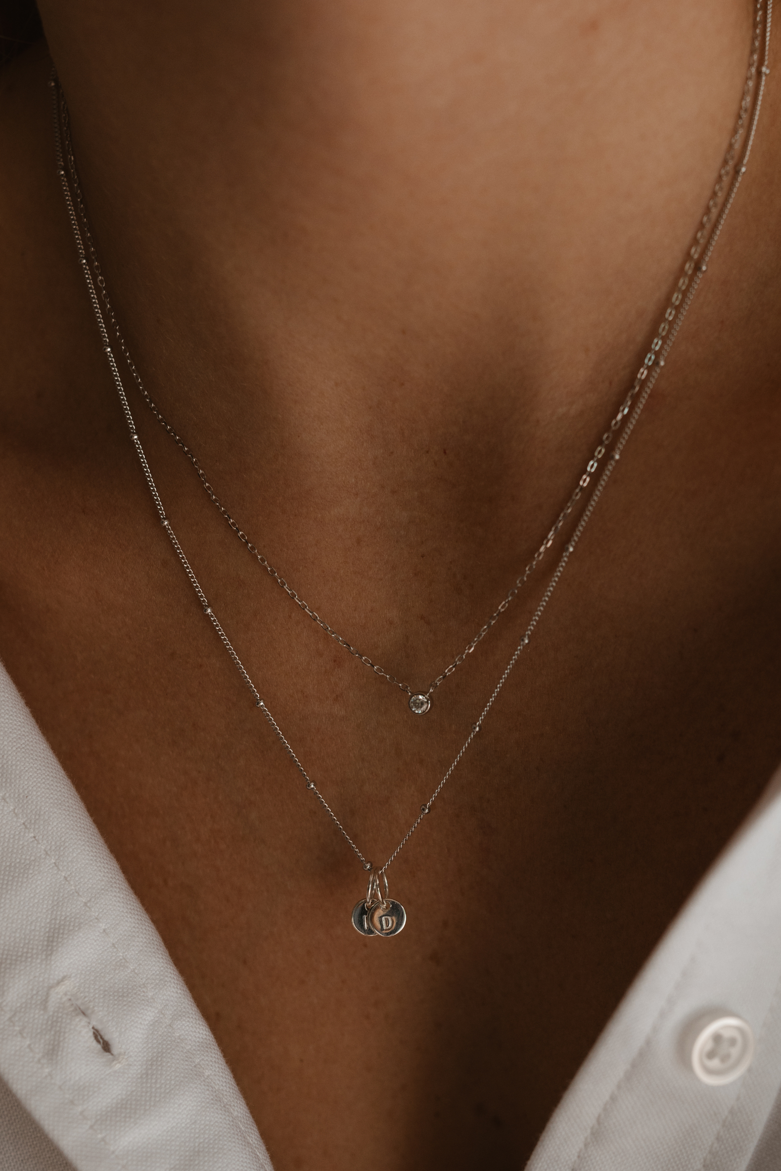 A woman wearing a silver Lumé Necklace by Bluebird Jewellery, inspired by the French word for ‘light’ and crafted as a meaningful fine jewellery gift. With matching personalised necklace with engraved pendants.